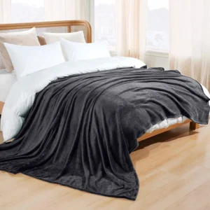 A dark grey fleece blanket draped over a white bed in a hotel bedroom.